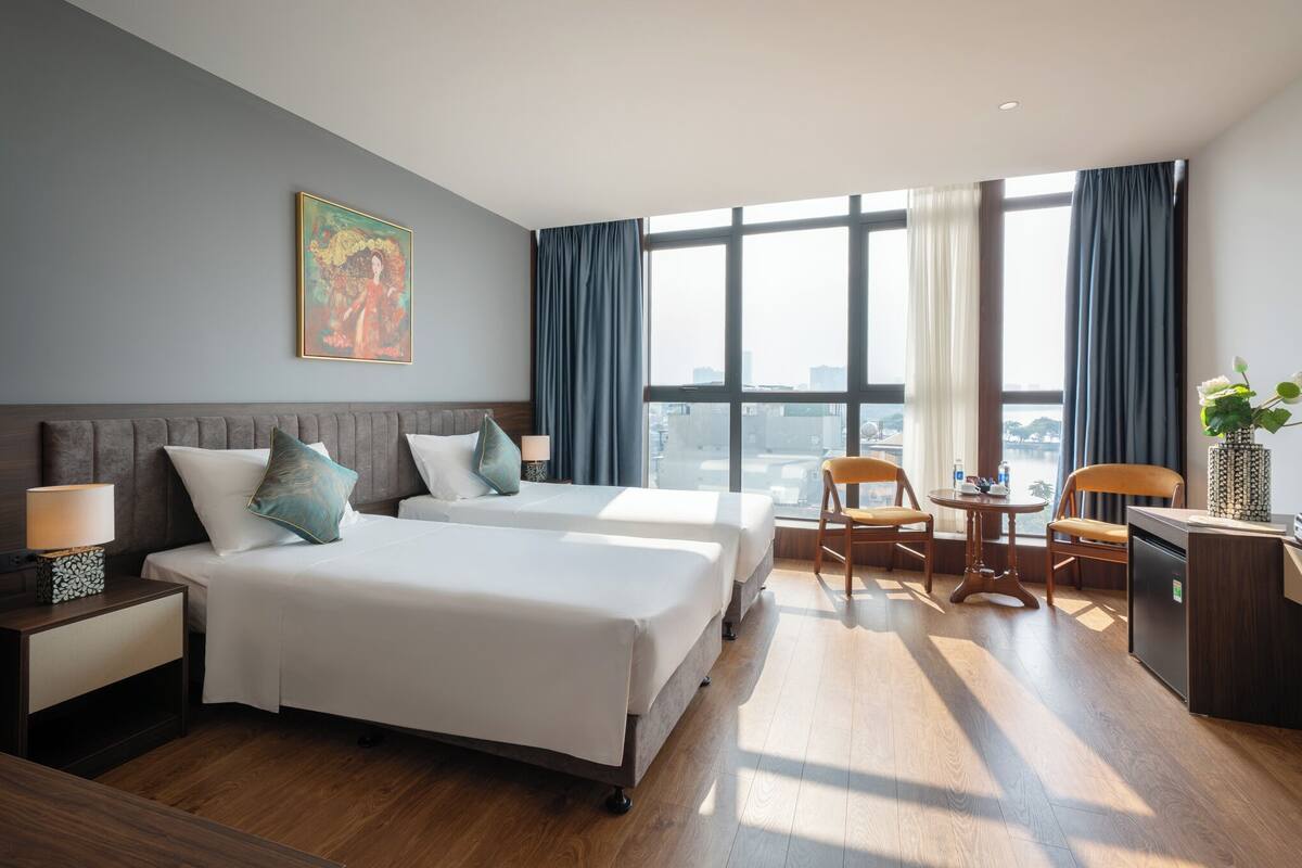 A hotel room with two beds, a desk, a chair, and a view of the city.