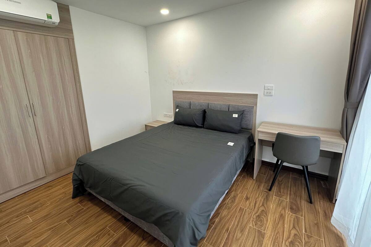 A bedroom with a bed, a desk, a chair, a wardrobe, and an air conditioning unit.