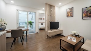 Een moderne hotelkamer met een houten vloer, een zithoek met een tafel en stoelen, een televisie op een standaard en kunstwerken aan de muren.