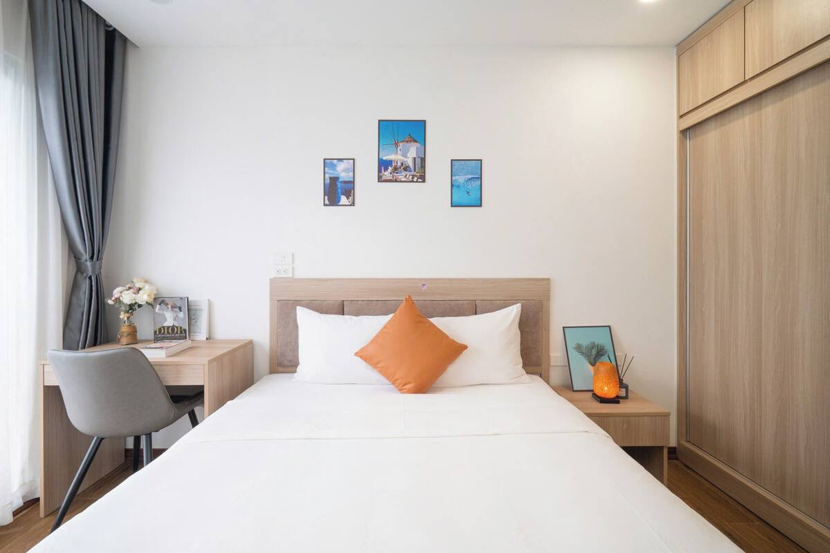 A hotel room with a bed, a desk, a chair, a nightstand, and three framed pictures on the wall.