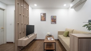 Een moderne woonkamer met een flatscreen televisie, houten planken, een salontafel met tijdschriften, een beige bank en een potplant.