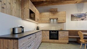 A modern kitchen with wooden cabinetry, a built-in oven, and a dining area with a bench. - Vacation apartment "Tischlerhof Alm" with balcony and mountain view (St.Jakob/Ahrntal)