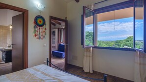 A bedroom with a bed, a window with a view, a dreamcatcher, and a bathroom visible through an open door.