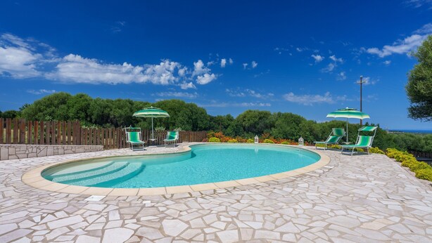 A swimming pool with a stone tile deck, surrounded by green chairs and umbrellas.
