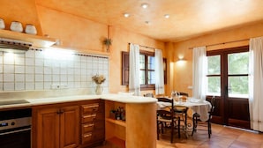 Cozinha com ilha central, armários de madeira, forno embutido e área de jantar com mesa e cadeiras.