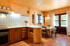 Una cocina con una isla central, armarios de madera, horno empotrado y un comedor con mesa y sillas.