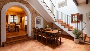 Uma área de refeições com um arco de pedra que dá para uma cozinha, uma escada com degraus de madeira e uma planta em vaso.