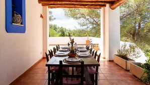 Uma sala de jantar com uma mesa posta para seis, cadeiras de madeira, uma prateleira azul fixada na parede e vista para árvores e céu.