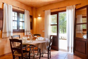 A dining area with a table set for four, chairs, a window with curtains, and a door leading outside. - Villa 'San Miguel Park' with Mountain View, Private Pool and Wi-Fi (Ibiza Town)