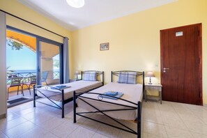 Ein Zimmer mit zwei Betten, einer Holztür, einem kleinen Tisch mit Lampe und einem Balkon mit Stühlen.