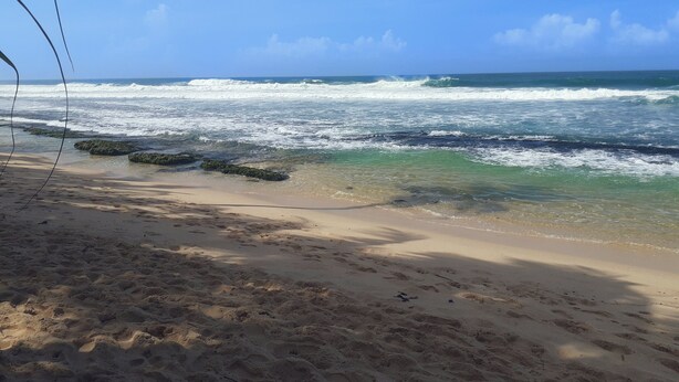 Une plage avec une eau d’un bleu limpide, un rivage sablonneux et des rochers dans l’eau.