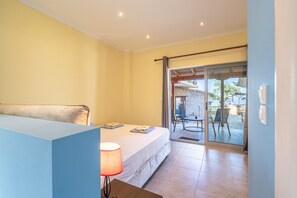Een slaapkamer met een bed, een nachtkastje met een lamp, een raam en een schuifdeur naar een buitenruimte met een tafel en stoelen.