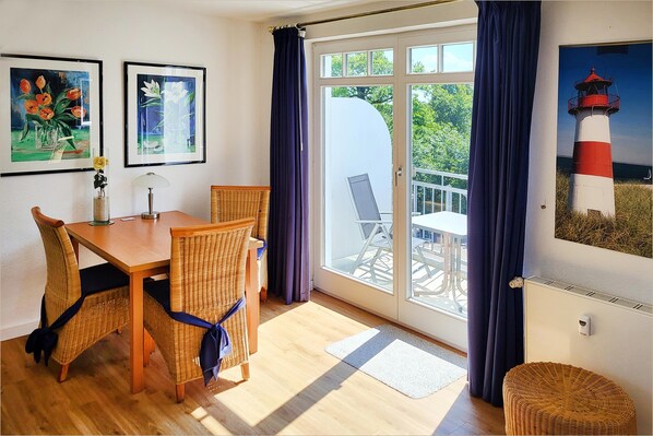 A room with a dining table, chairs, a window with curtains, and artwork on the walls.