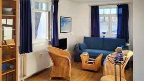 Ein Wohnzimmer mit einem blauen Sofa, Korbstühlen, einem kleinen Tisch und einem Bücherregal.