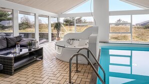A modern indoor pool area with a jacuzzi, a lounge area with a sofa and coffee table, and large windows offering a view of the surrounding landscape. - "Caya" - 750m from the sea by Interhome (Løkken)