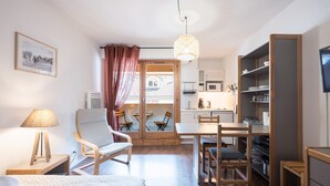 A compact room with a bed, a desk, a chair, a dining table, and a kitchenette.