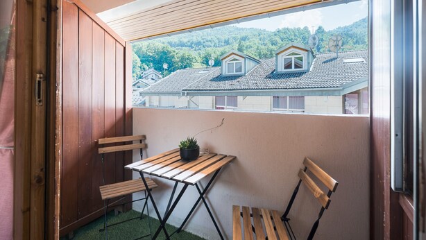 A balcony with a wooden table, two chairs, and a potted plant.