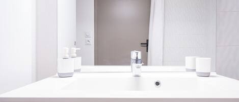 Un baño moderno con lavamanos blanco, un espejo y una puerta con perchero para toallas.