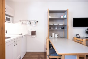 Uma cozinha compacta com armários brancos, micro-ondas, pia e uma mesa de madeira com uma cadeira.