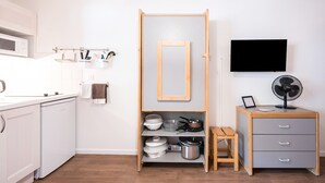 A kitchen with white cabinets, a microwave, a wooden shelf with dishes, a small table, and a grey drawer unit.