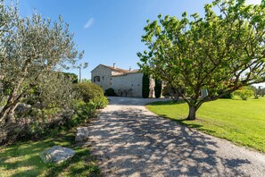 A stone building with a gravel driveway, surrounded by greenery and trees.