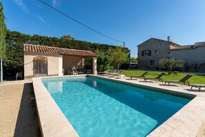 A swimming pool with lounge chairs, a covered seating area, and a stone building in the background.