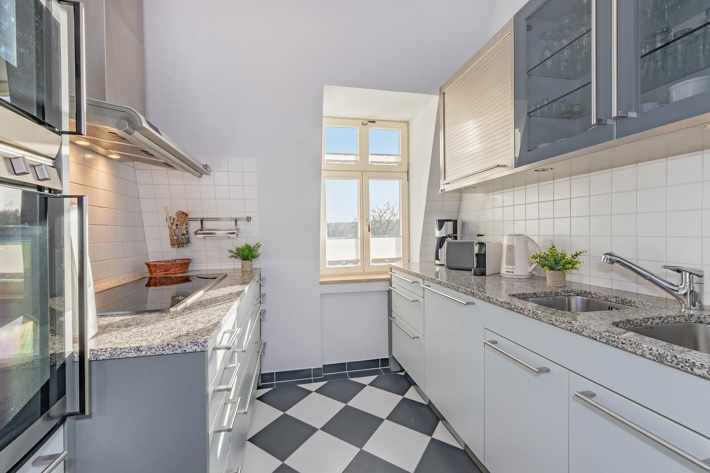 Una cocina moderna con armarios blancos, encimeras de granito y suelo a cuadros blanco y negro.