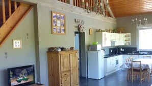 A spacious living area with a wooden staircase, a television, a dining table with chairs, and a kitchen area.