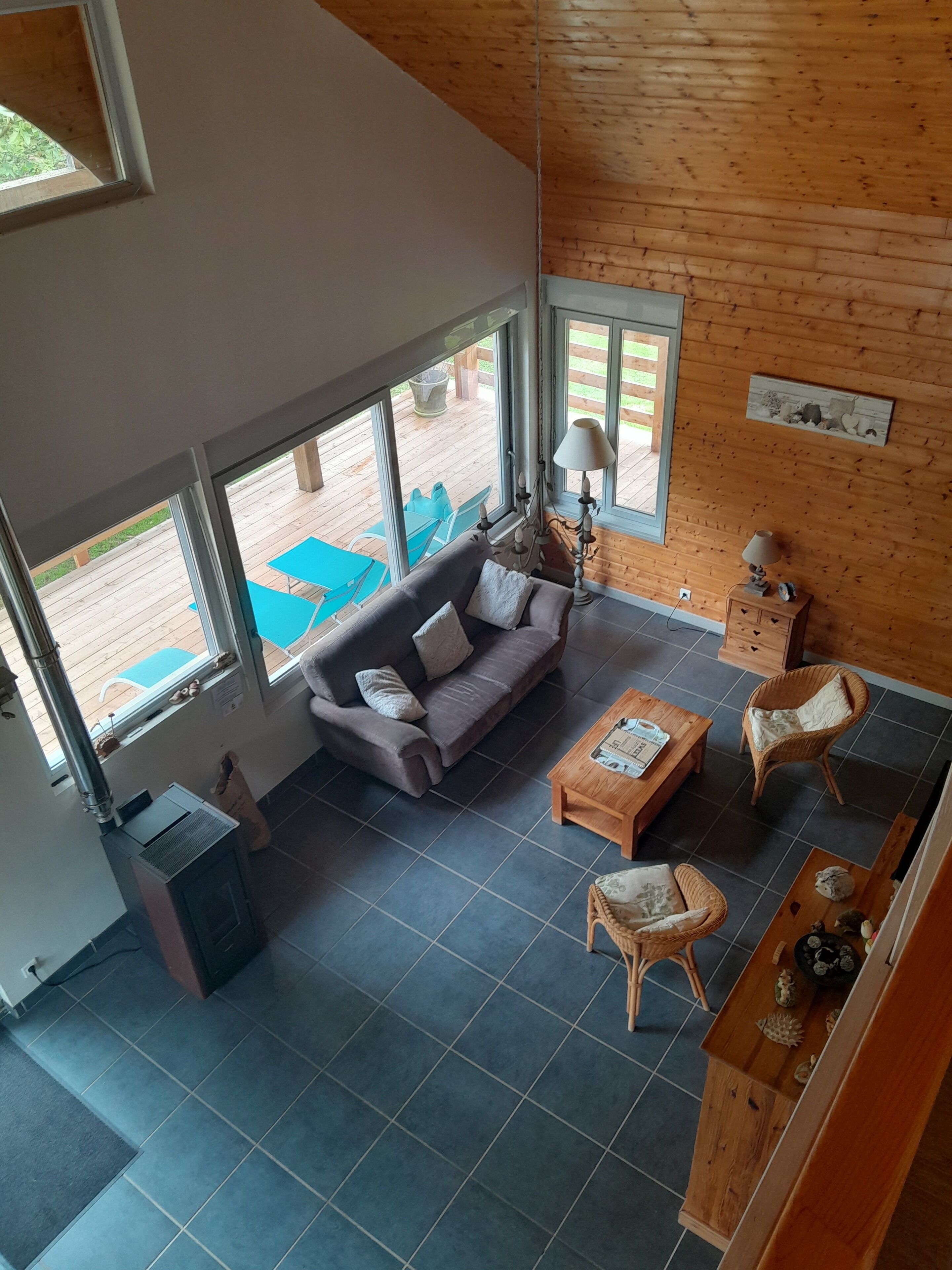 A spacious living area with a sofa, coffee table, and wicker chairs. Large windows provide views of an outdoor deck.