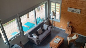 A spacious living area with a sofa, coffee table, and wicker chairs. Large windows provide views of an outdoor deck.