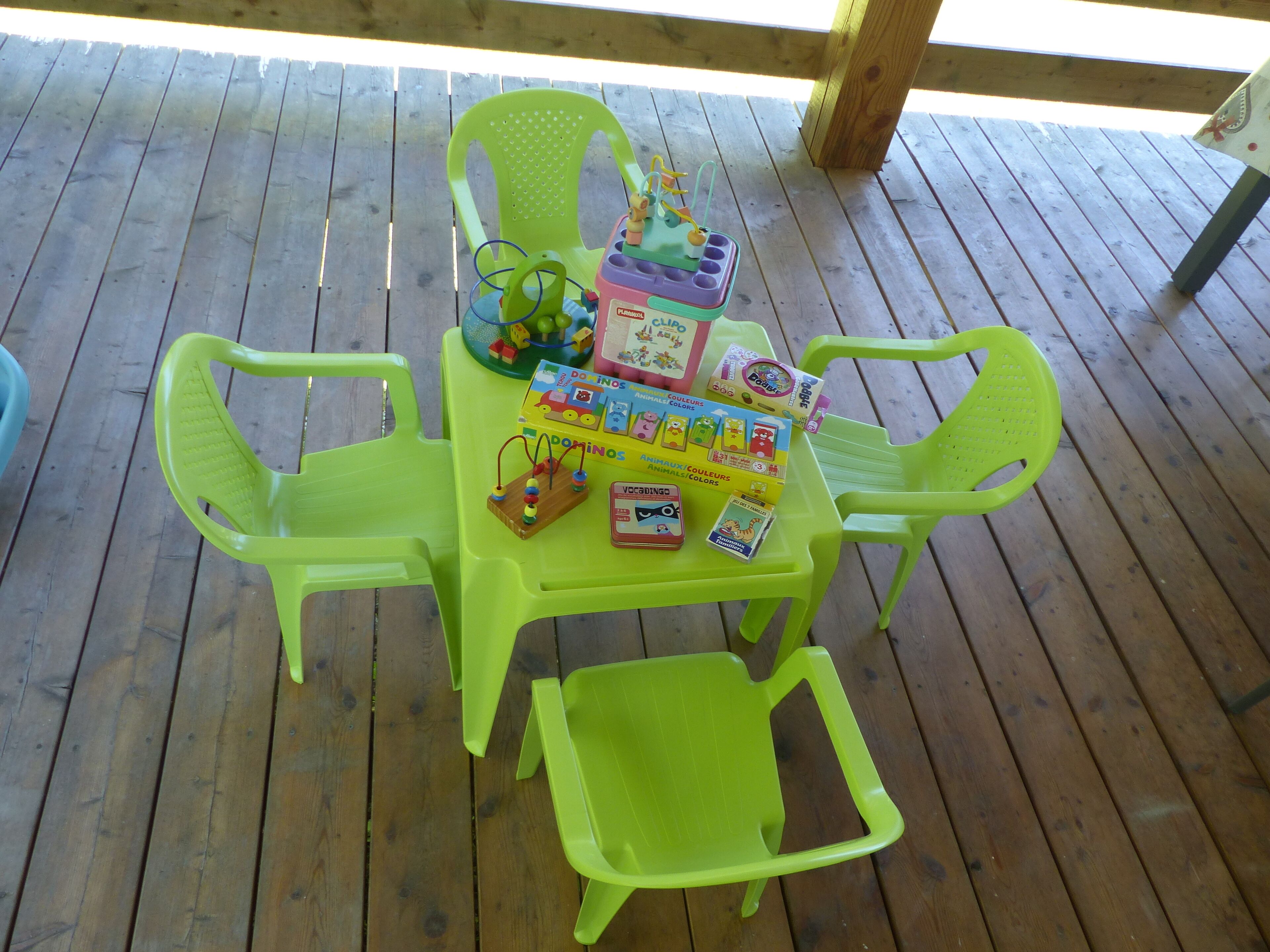 Eine Holzterrasse mit einem Tisch und vier grünen Plastikstühlen.