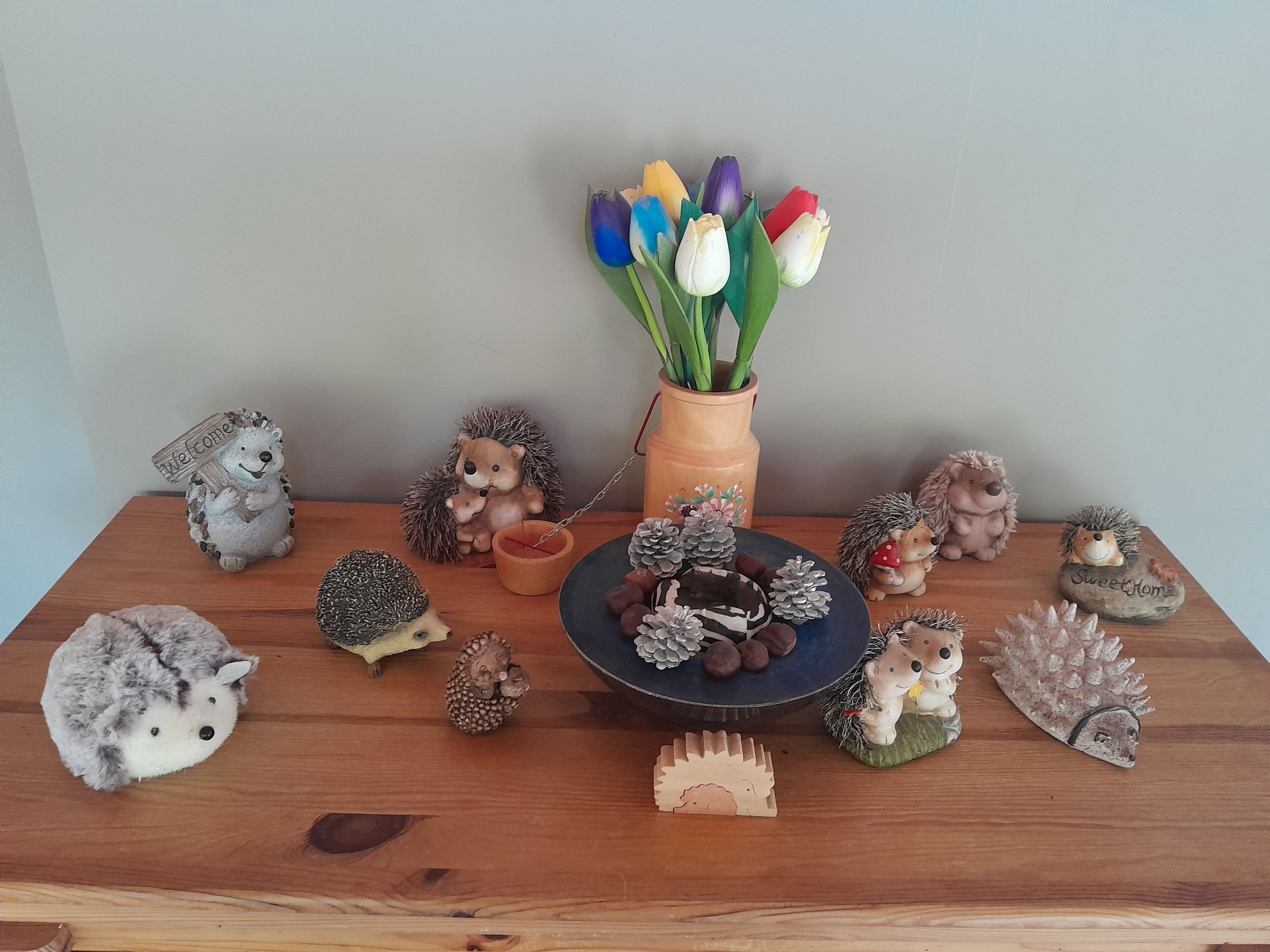 A wooden table with various hedgehog figurines and a vase of tulips.