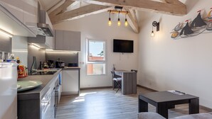 A modern kitchen with a built-in oven, a dining area with a table and chairs, a flat-screen TV mounted on the wall, and a wooden ceiling with exposed beams. - Bright, Newly Renovated Apartment with Wi-Fi and Air Conditioning (Sanary-sur-Mer)