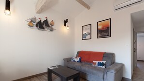 A living room with a grey sofa, a small table, wall art, and a ceiling with exposed beams. - Bright, Newly Renovated Apartment with Wi-Fi and Air Conditioning (Sanary-sur-Mer)