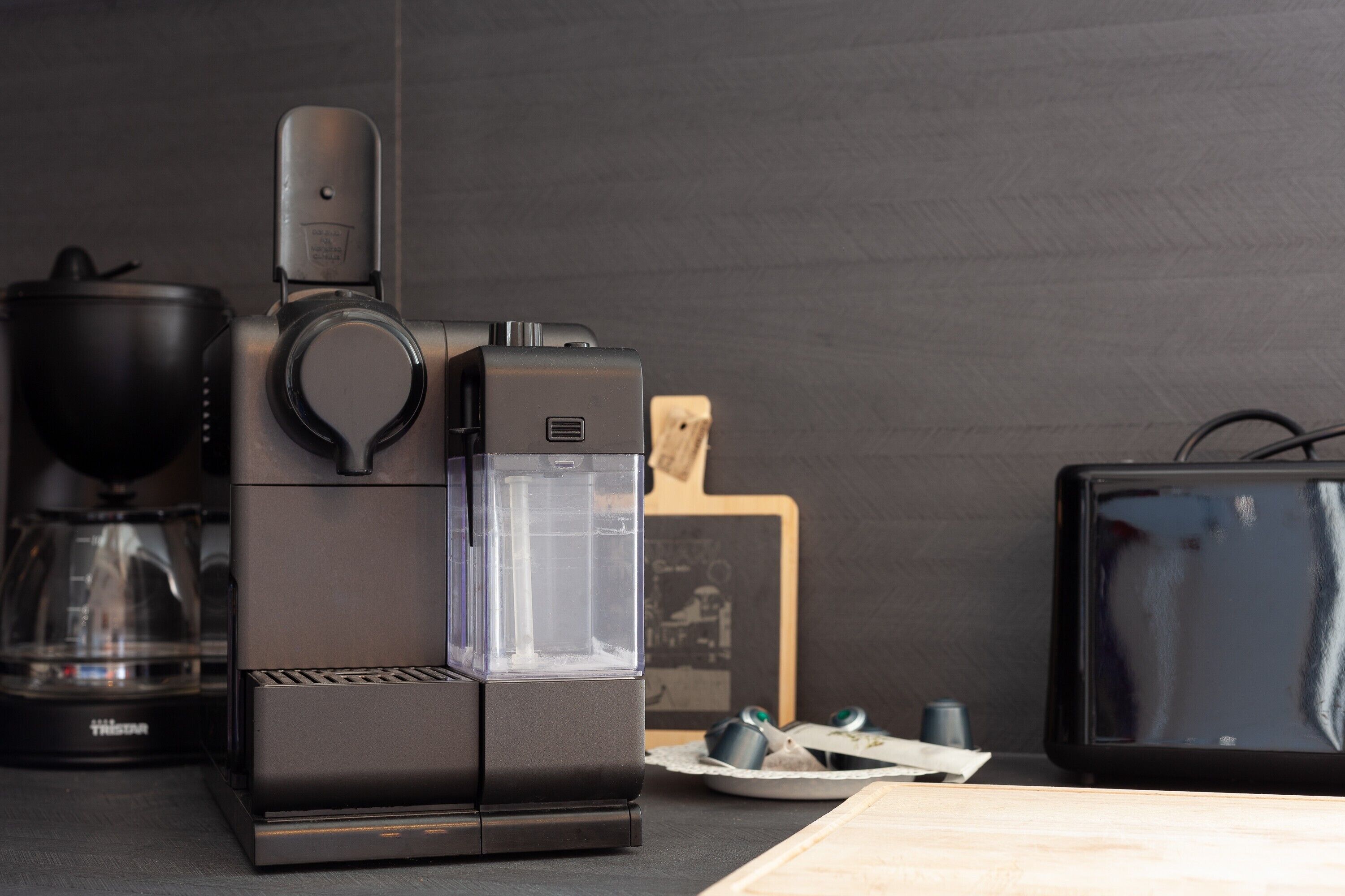 A coffee maker, a glass carafe, a wooden cutting board, and a television on a kitchen counter.