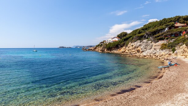 A coastal beach with clear water, a boat, and houses on a hillside. - Bright, Newly Renovated Apartment with Wi-Fi and Air Conditioning (Sanary-sur-Mer)