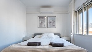 A bedroom with a bed, two framed artworks, a window, and a wall-mounted air conditioner. - Apartment 'Penthouse In Old Town' with Panoramic Sea and Mountain Views, Wi-Fi and Air Conditioning (Fuengirola)