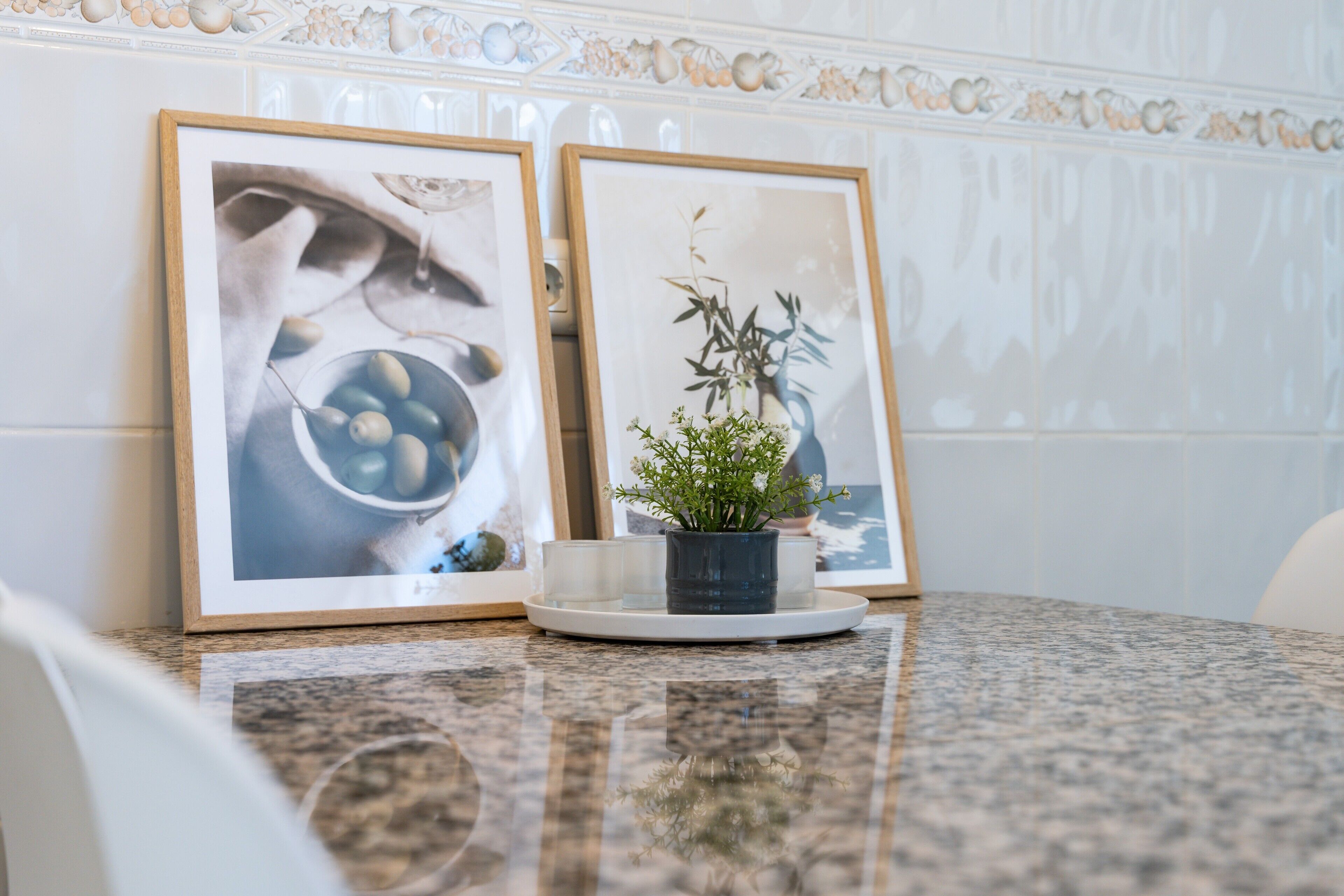 A framed picture of olives and a potted plant on a marble countertop.