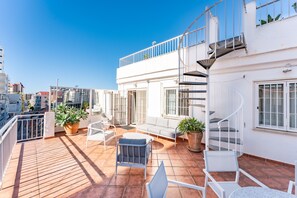 Terraza en la azotea con mobiliario exterior, plantas en macetas y una escalera de caracol.