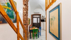 A narrow hallway with a staircase, a dining area with chairs and a table, and artwork on the walls.