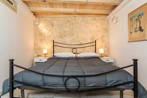 Un lit avec un cadre en métal, deux tables de chevet avec des lampes, un mur en pierre et un tableau accroché au mur.