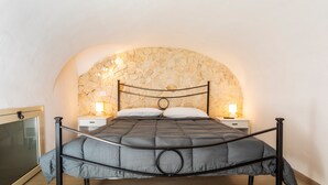 A bed with a headboard, two bedside tables, and a stone wall arch.