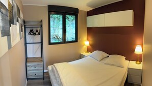 A bedroom with a bed, two bedside lamps, a window with a view of greenery, a wooden dresser, and a wall-mounted shelf with shoes. - La tiny T Loches, close to Beauval Zoo and the Châteaux. (Loches)