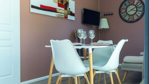 A dining area with a table set for two, white chairs, and a wall-mounted TV. - La tiny T Loches, close to Beauval Zoo and the Châteaux. (Loches)