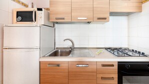 A kitchen with a microwave, stove, sink, and wooden cabinets. - Apartment 'Di Titina' with Private Terrace and Air Conditioning (Otranto)