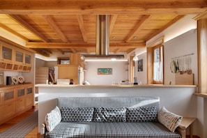 A cozy room with a sofa, wooden cabinets, a kitchen area, and a large window.