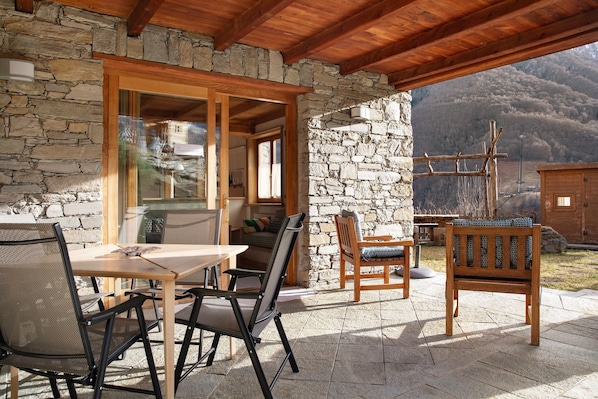 An outdoor patio with stone walls, wooden furniture, and a view of mountains.