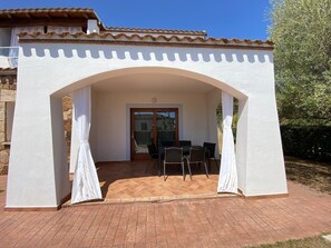 Un patio techado con una mesa y sillas, una puerta que da a un acceso cubierto y un techo de baldosas.