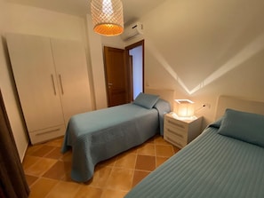 Une chambre avec deux lits, une armoire, une table de chevet avec une lampe et un appareil de climatisation.