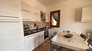 Uma cozinha compacta com armários brancos, fogão, pia e uma mesa de jantar com cadeiras.